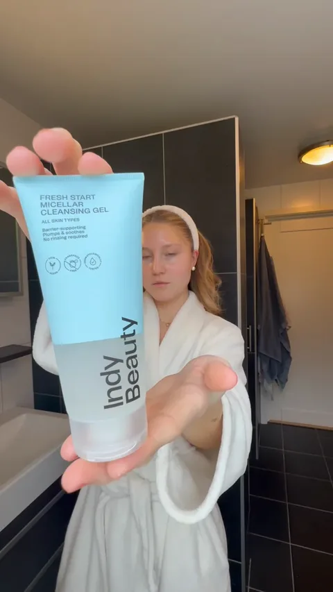 A creator in a bathrobe holding Indy Beauty Fresh Start cleansing gel in her bathroom