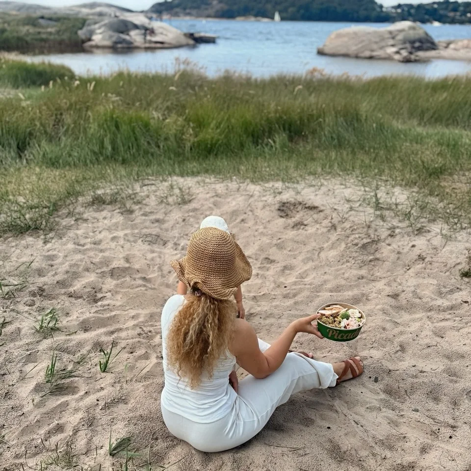 A creator in a sun hat with a Picadeli bowl on a sandy beach by the sea