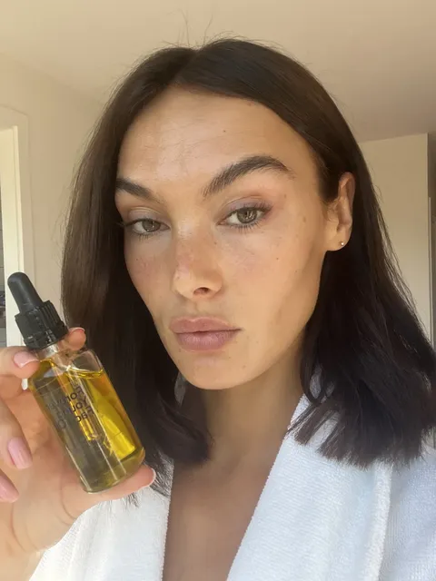 Creator holding face oil in a white robe