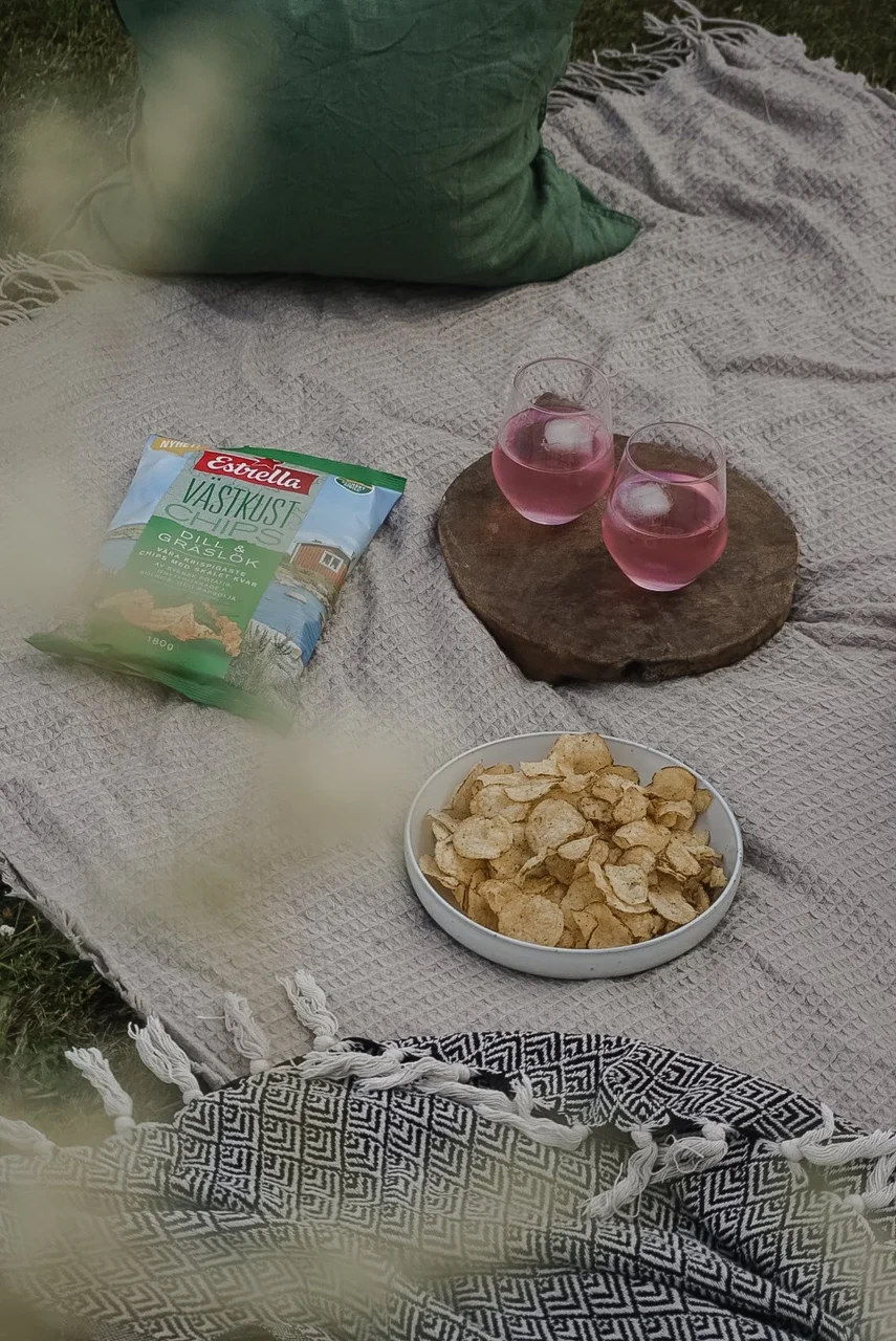 Estrella snacks on a picnic blanket with drinks and a bowl of crisps