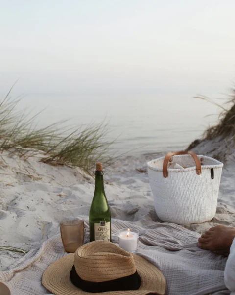 Drinks and a picnic basket on a blanket by the sea