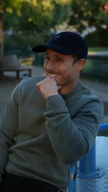 Creator wearing a grey sweater and a cap outdoors