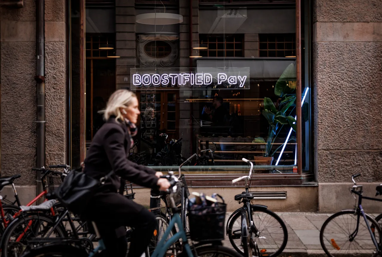 Skylten ”BOOSTIFIED – Betala” i ett skyltfönster, med cyklar utanför.