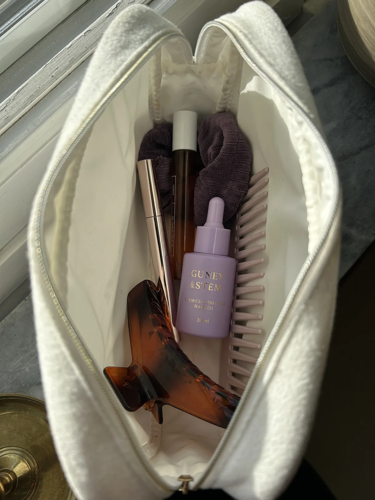 Guney & Stem hair oil in a toiletry bag with hair accessories