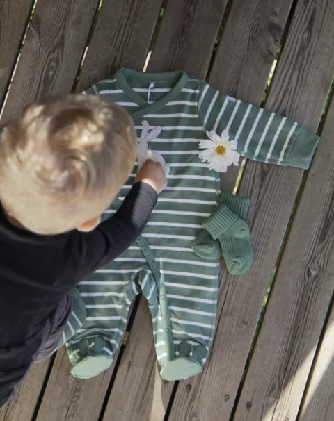 Child beside striped green baby clothes