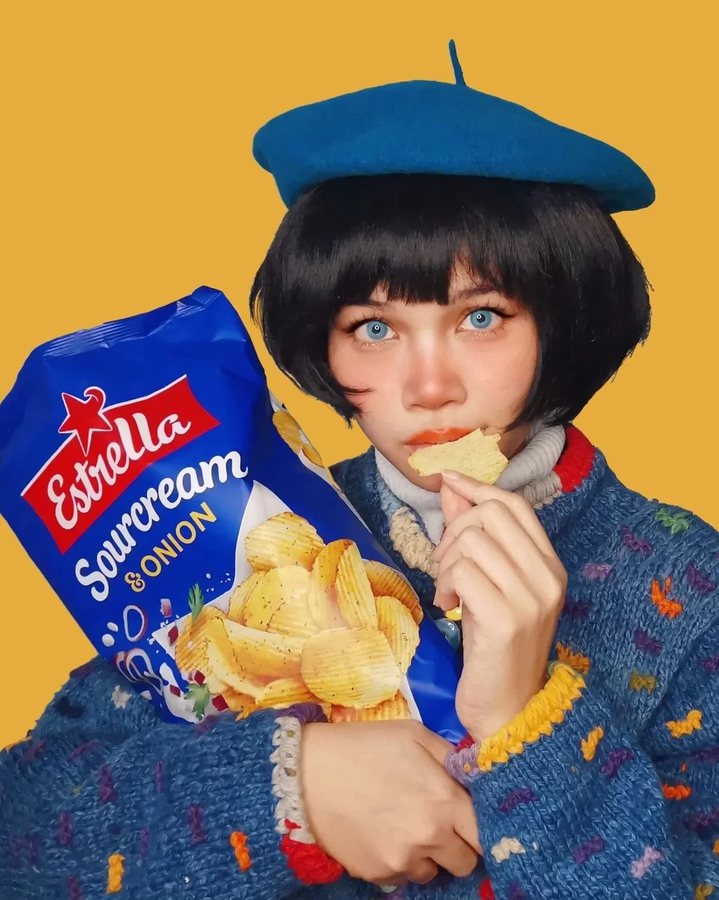 Creator wearing a blue beret and holding Estrella Sourcream and Onion crisps